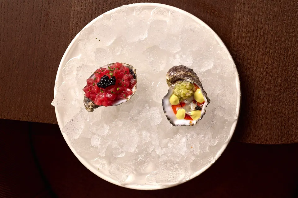 Dos ostras sobre hielo con aliños servidas en plato blanco