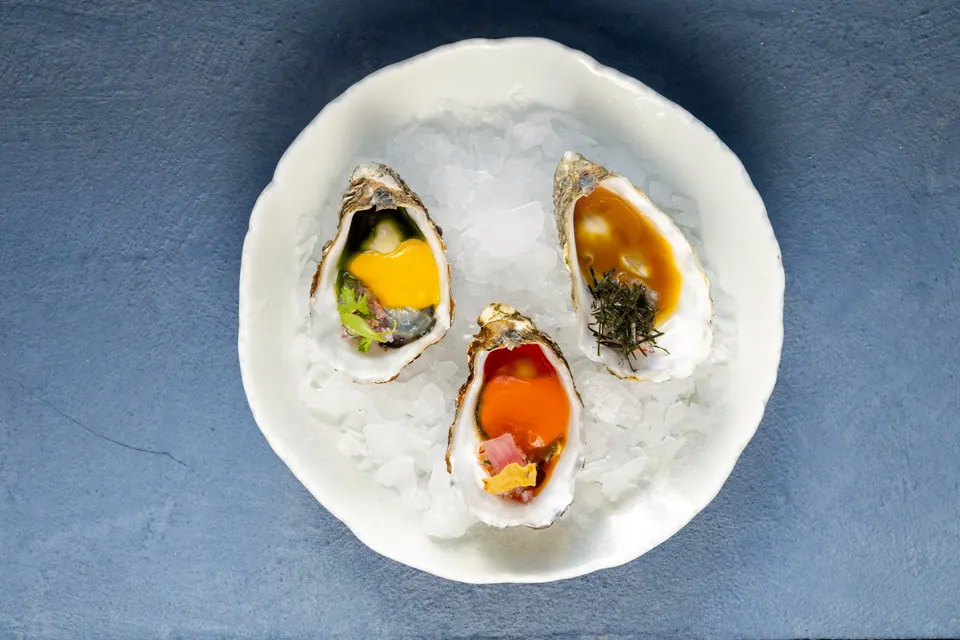 Tres ostras aliñadas servidas sobre hielo en un plato blanco