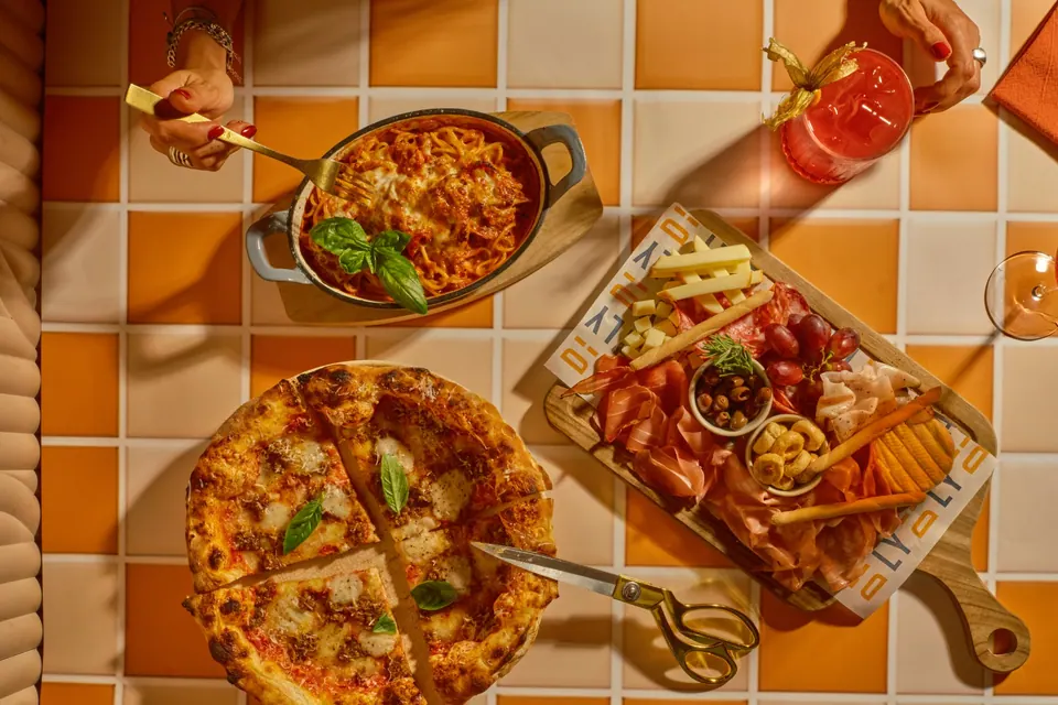 Pizza, pasta gratinada, tabla italiana y bebida sobre mesa de Ditaly