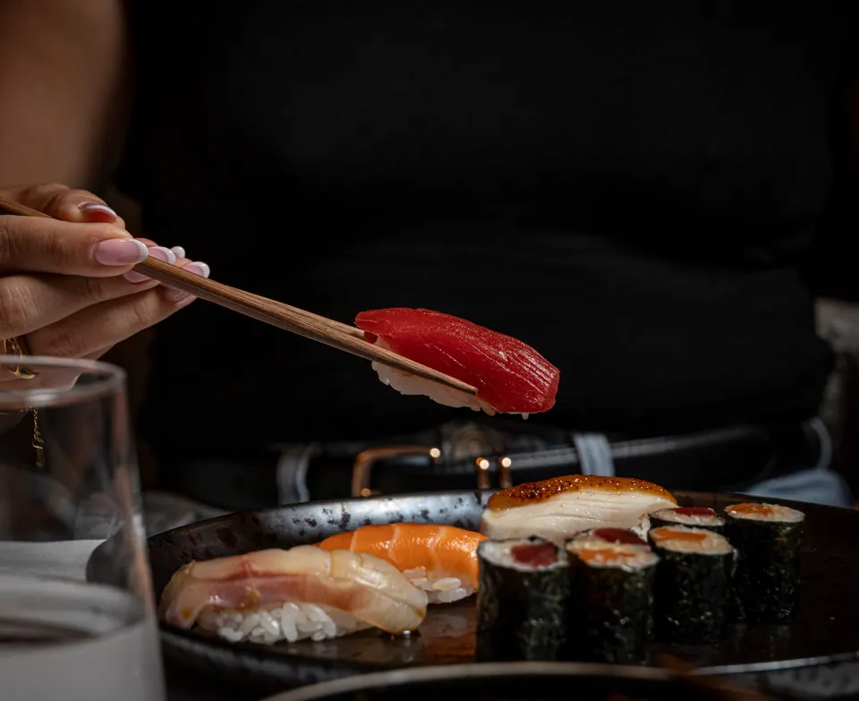 Comensal tomando un nigiri de atún con palillos sobre bandeja de sushi