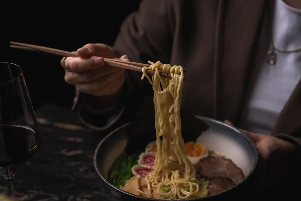 Comensal tomando fideos ramen con palillos en una mesa de Os-kuro